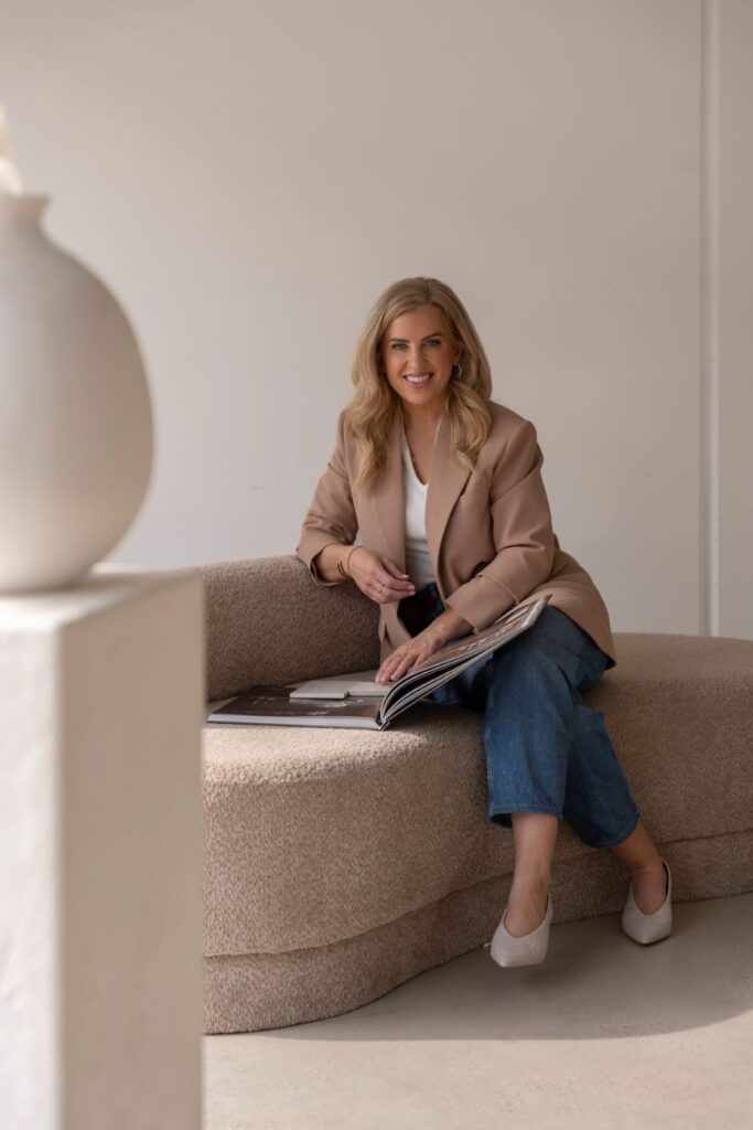 Mary O’Loughlin sitting on a curved sofa with renovation plans in a neutral interior.