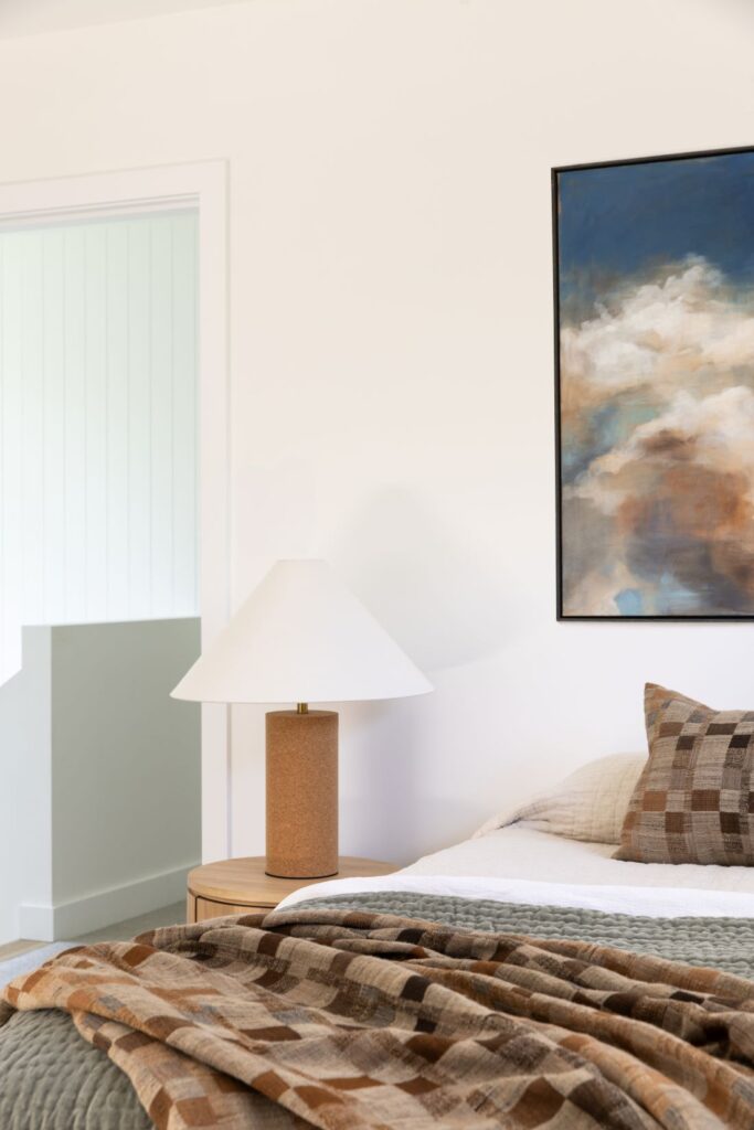 Waterhousia bedroom with brown checked bedding, textured neutral cushions, a cork-base bedside lamp and large abstract artwork above the bed.