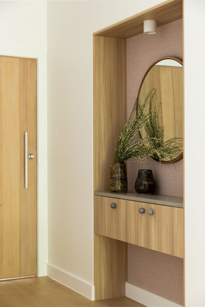 Waterhousia entryway featuring built-in timber joinery, curved mirror, textured wall finish, decorative vases and warm neutral styling.