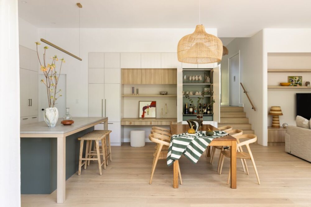 Waterhousia open plan kitchen and dining area featuring white cabinetry, timber accents, woven pendant light, timber dining table and neutral coastal-inspired styling.