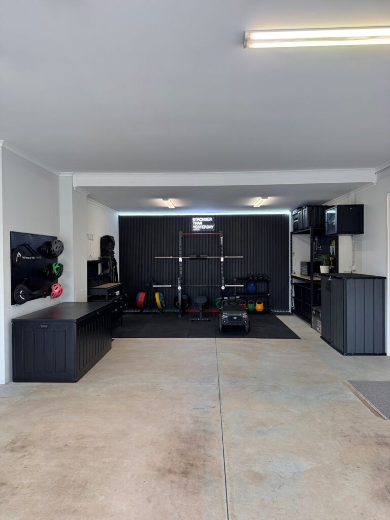 Organised garage featuring black storage cabinets, wall-mounted equipment racks, shelving and a designated workout area.