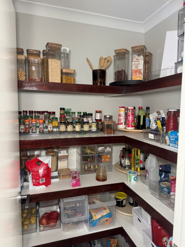 Pantry before organisation with shelves filled with jars, bottles, food items, containers and kitchen supplies.