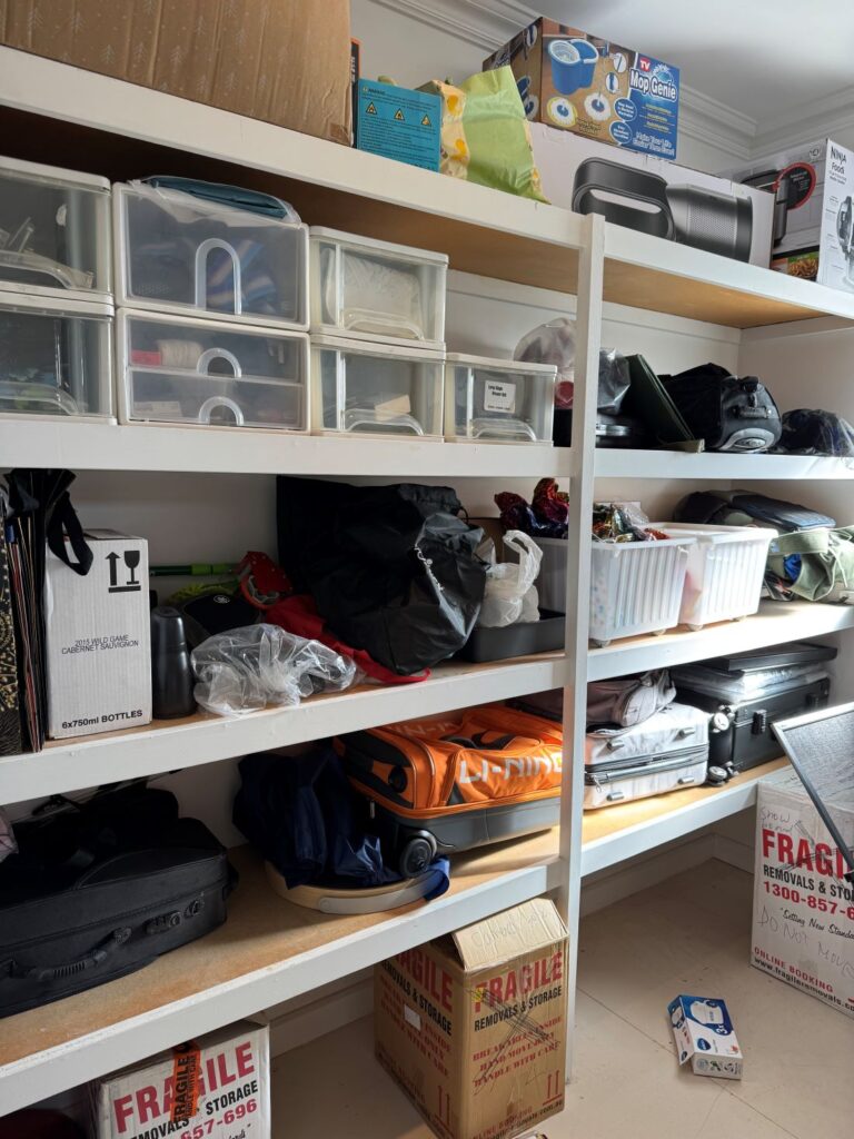 Storage room before organisation with shelves containing boxes, luggage, storage containers, bags and household items.
