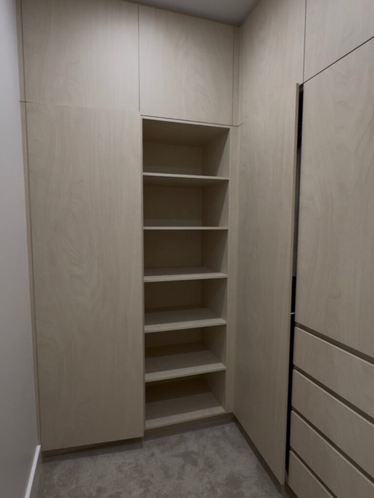 Empty walk-in wardrobe before organisation featuring built-in cabinets, open shelves, drawers and neutral wood finishes.