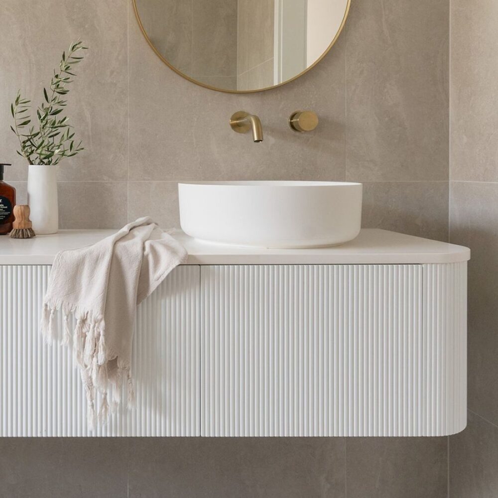 White fluted floating vanity with round gold mirror